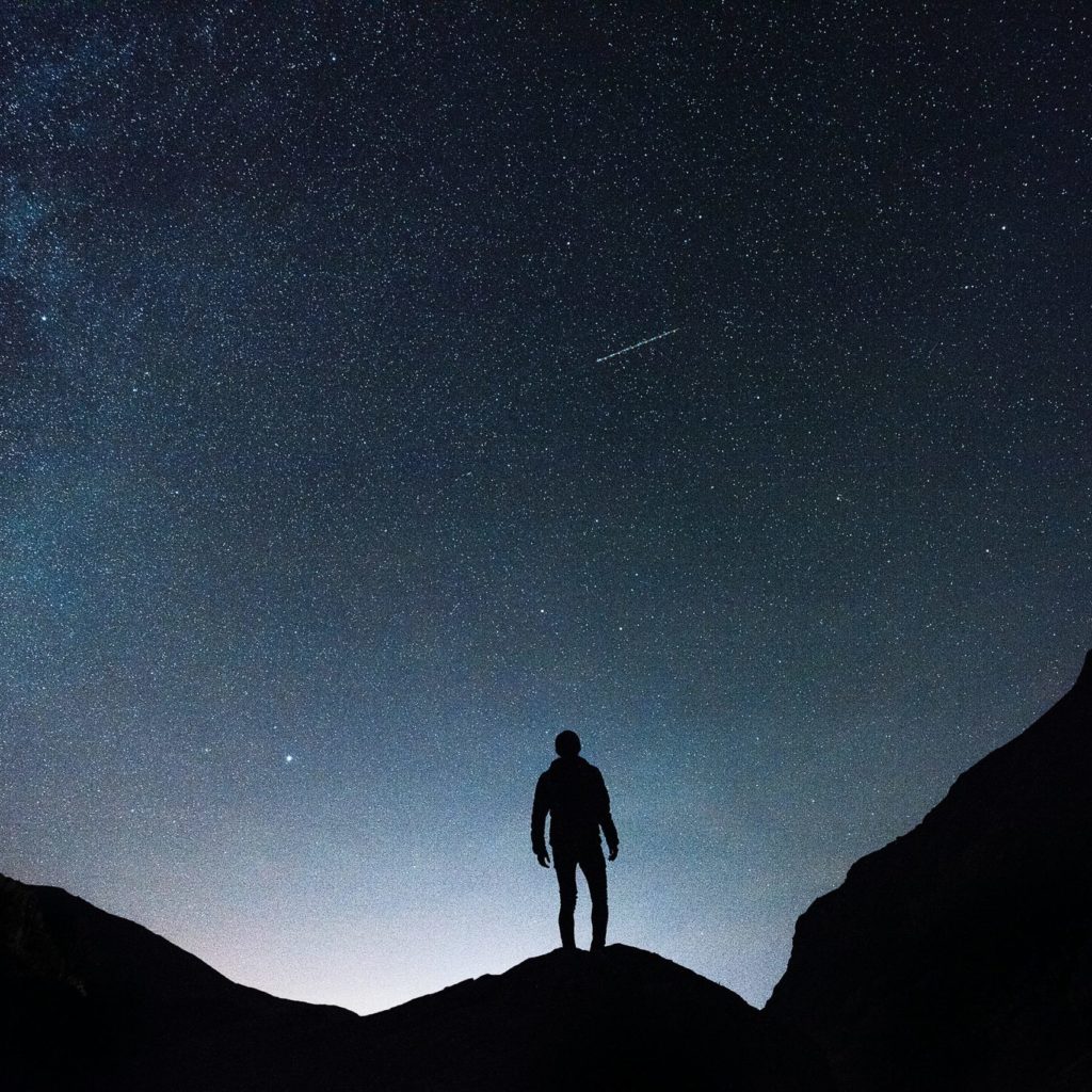 Uomo sul picco di un monte, guarda il cielo stellato con una cometa.