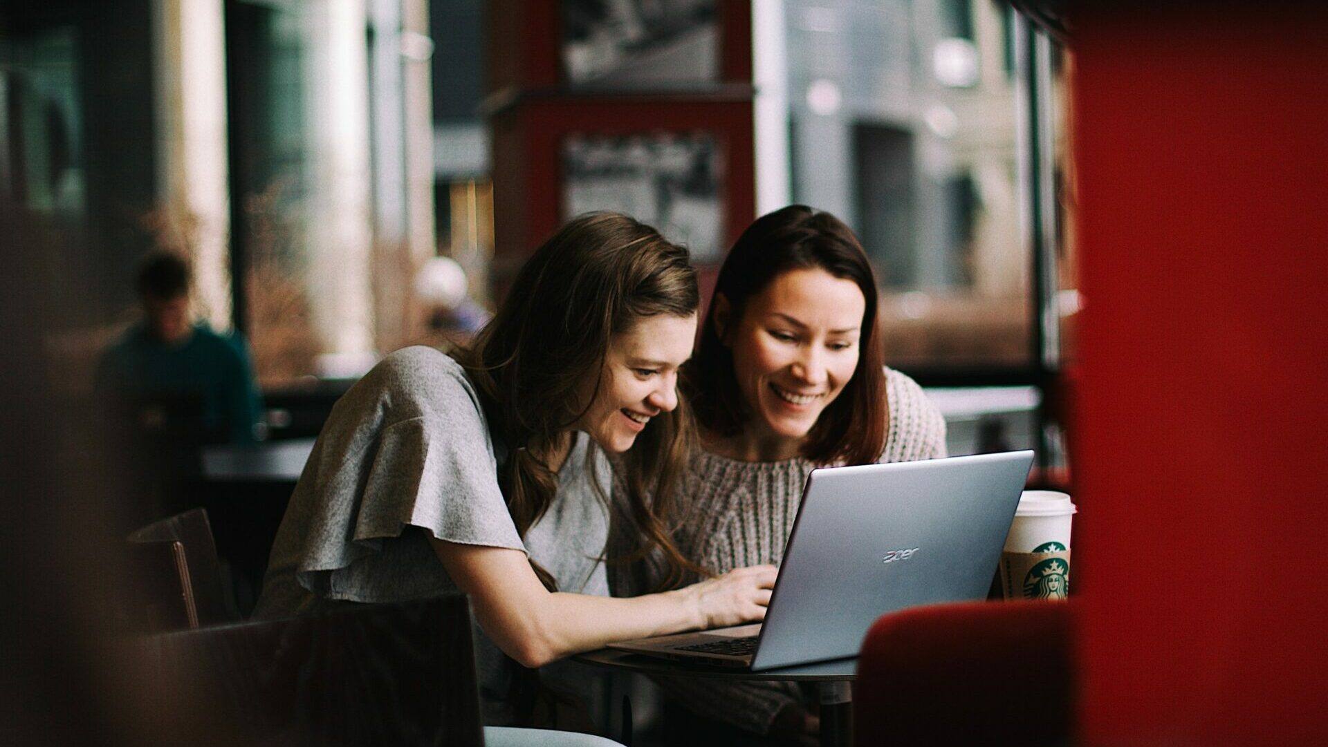 foto di una ragazza e una donna più grande sedute a un bar che guardano qualcosa al computer e sorridono